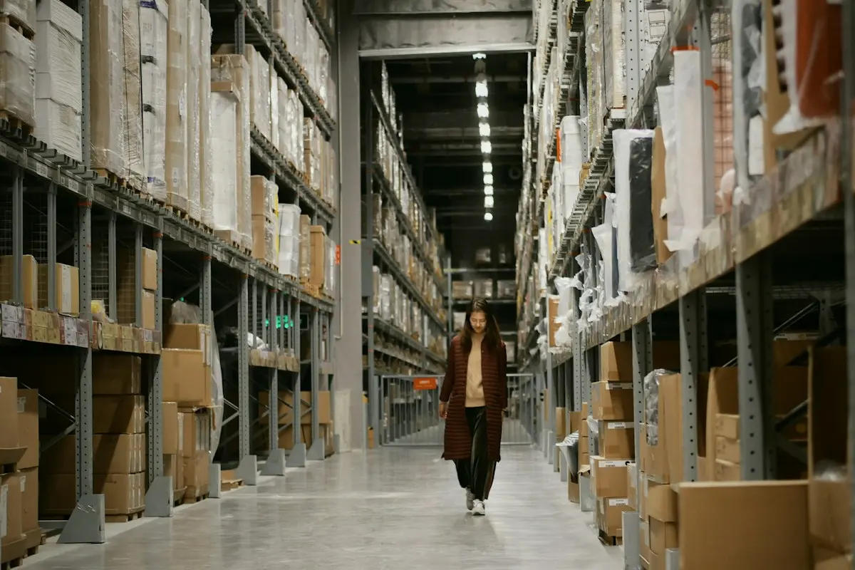 Worker walking down a warehouse aisle between tall stock racks