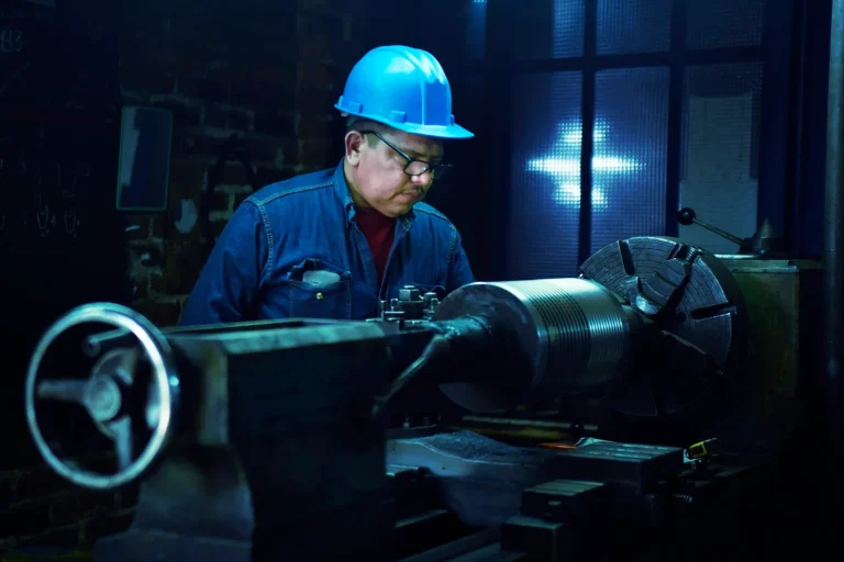 Machine operator in a hard hat working at a metal lathe